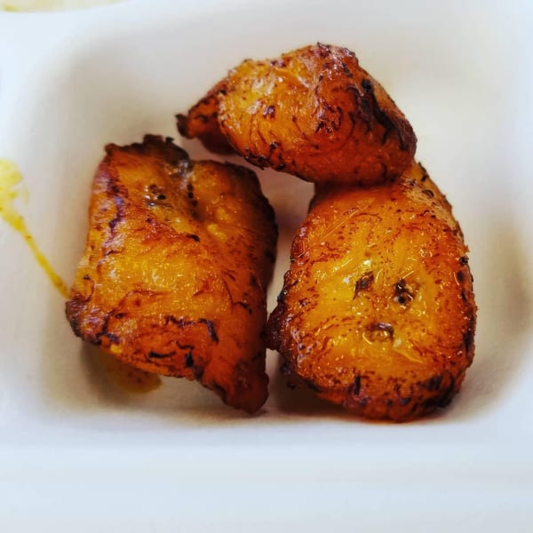 Three golden-brown fried plantains with caramelized edges, served in a white dish.