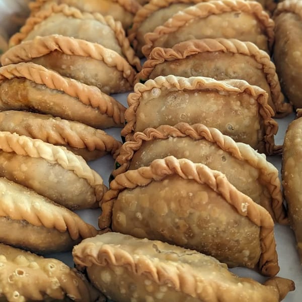 Close-up of many golden-brown Puerto Rican empanadillas with crimped edges, arranged on a white surface.