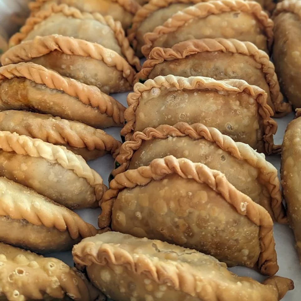 Close-up of many golden-brown Puerto Rican empanadillas with crimped edges, arranged on a white surface.