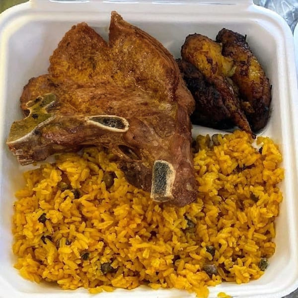 A Puerto Rican meal with a large pork chop, yellow rice with beans, and fried plantains.