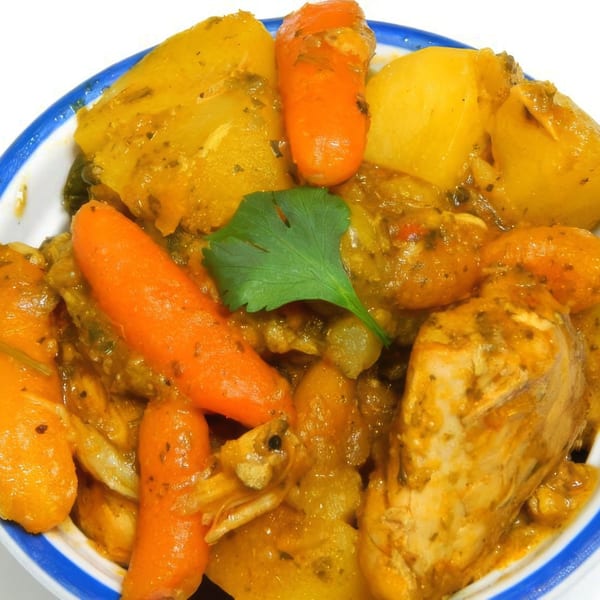 Close-up of Puerto Rican chicken stew with potatoes, carrots, and cilantro in a white and blue bowl.