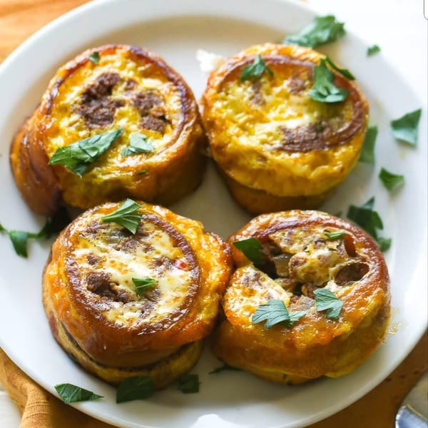 Four savory Puerto Rican plantain and egg muffins with meat filling, garnished with fresh herbs.