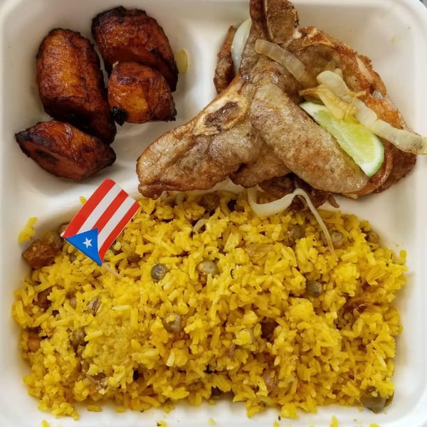 Puerto Rican meal with fried pork chop, yellow rice, plantains, and a small Puerto Rican flag.